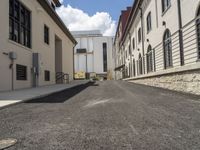 an empty street in the middle of a residential neighborhood with old buildings lining each side and a bench on the far side