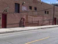 a sidewalk next to a fire hydrant near the side of a brick building with a sign hanging out the middle of it