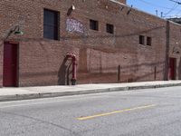 a sidewalk next to a fire hydrant near the side of a brick building with a sign hanging out the middle of it