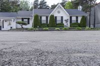 a house on the corner of a road and in front of a tree line and bushes