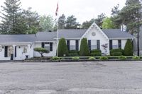 a house on the corner of a road and in front of a tree line and bushes