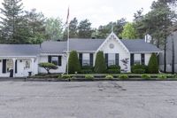 a house on the corner of a road and in front of a tree line and bushes