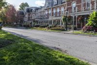 a street lined with parked cars near a tall brick building and lawn area with colorful flowers in the foreground