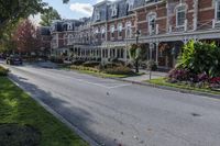 a street lined with parked cars near a tall brick building and lawn area with colorful flowers in the foreground