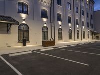 an empty parking lot outside a building lit up at dusk, with lights on the windows