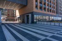 a walkway in front of a modern building with many windows, and a man on a bike