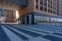 a walkway in front of a modern building with many windows, and a man on a bike