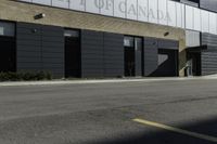 a motorcycle rider travels past a large building in a parking lot, with the city in the background