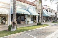 palm trees are growing around some white buildings in the city street, along the sidewalk