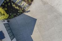 an aerial shot of concrete courtyard, and bench on sidewalk area with bushes in background