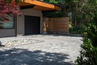 the driveway has some stone on it next to trees and bushes on the sidewalk of this home