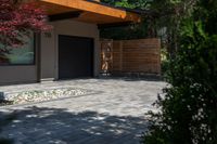 the driveway has some stone on it next to trees and bushes on the sidewalk of this home