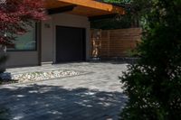 the driveway has some stone on it next to trees and bushes on the sidewalk of this home