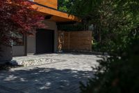 the driveway has some stone on it next to trees and bushes on the sidewalk of this home