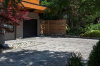 the driveway has some stone on it next to trees and bushes on the sidewalk of this home