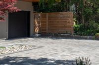 the driveway has some stone on it next to trees and bushes on the sidewalk of this home