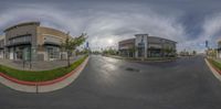 an asphalt street with a shopping center and a cloudy sky overhead at the camera taken from the same angle