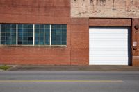 two garage doors and an empty street in front of an old building with a white door