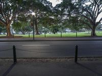 the road is empty in front of a tree filled park area with benches and tables