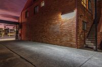 a dark, concreteed street has stairs and windows at sunset in a red brick building