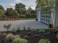 a driveway in front of a garage next to a tree and shrubbery area outside