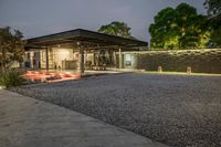 a home with lots of landscaping and gravel on the driveway area at night time with red car