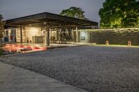 a home with lots of landscaping and gravel on the driveway area at night time with red car