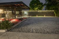 a gravel yard, with a stone walkway in front of it, leads to a modern glass front patio