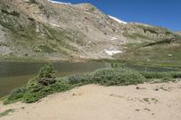 a person with a hat on is standing by a mountain lake in the mountains with a bike rack