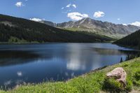 an alpine lake surrounded by forested mountains on the road to the mountaintop, in the summer