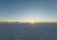 the view of the sun over a field with footprints in the sand and hills in the distance