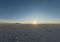 the view of the sun over a field with footprints in the sand and hills in the distance