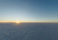 the sun shines over the horizon of a vast winter plain with footprints across a snow covered field