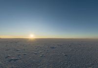 the sun shines over the horizon of a vast winter plain with footprints across a snow covered field