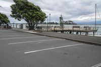 a person standing on a bench next to the water and pier near trees and a fence