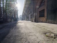 a street with concrete sidewalk and brick building with the sun in background and light reflecting through the window