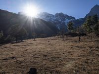 the sun shining over the mountains behind the field and trees in the foreground of the scene