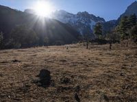 the sun shining over the mountains behind the field and trees in the foreground of the scene