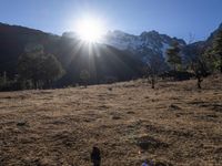 the sun shining over the mountains behind the field and trees in the foreground of the scene