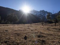 the sun shining over the mountains behind the field and trees in the foreground of the scene