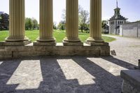 the sun is streaming through the pillars of a building, surrounded by grass and a grassy field