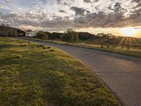 a picture of the sun shining down on some grass and houses by the road on the other side