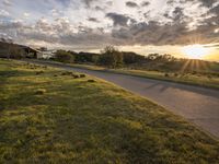 a picture of the sun shining down on some grass and houses by the road on the other side