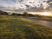 a picture of the sun shining down on some grass and houses by the road on the other side