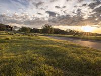 a picture of the sun shining down on some grass and houses by the road on the other side