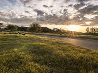 a picture of the sun shining down on some grass and houses by the road on the other side