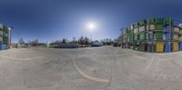 a fish eye view shows an empty parking lot in the sun and buildings in the background