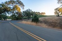 a motorcycle driving on a country road in the daytime sun with trees to the side of it