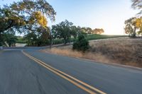 a motorcycle driving on a country road in the daytime sun with trees to the side of it