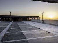 an empty parking lot with buildings and light poles in the background at sunset, in the evening